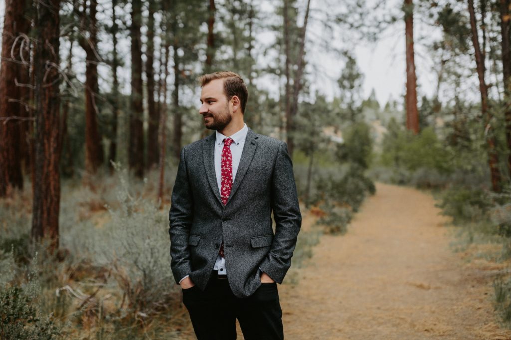 groom in the forest on wedding day with grey suit and red tie