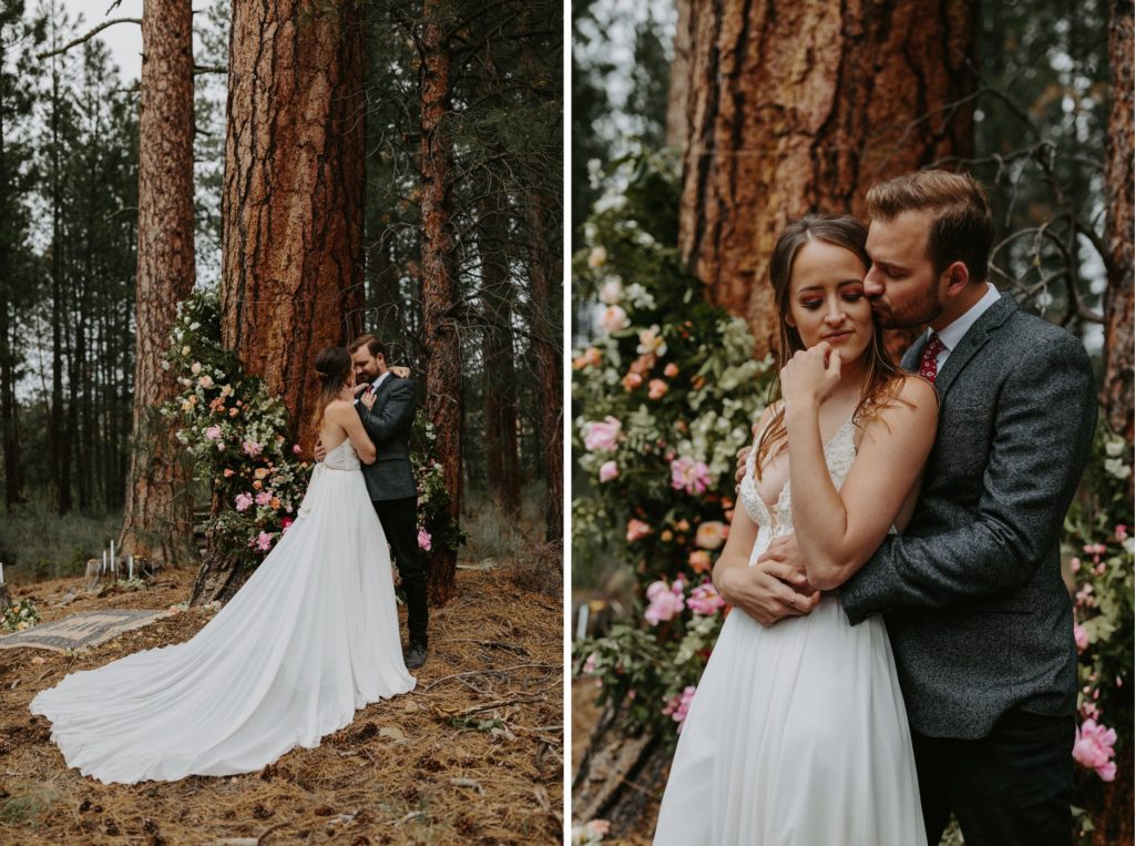 bride in white flowy dress and groom in grey suit in front of their floral ceremony arch for their woodsy forest wedding