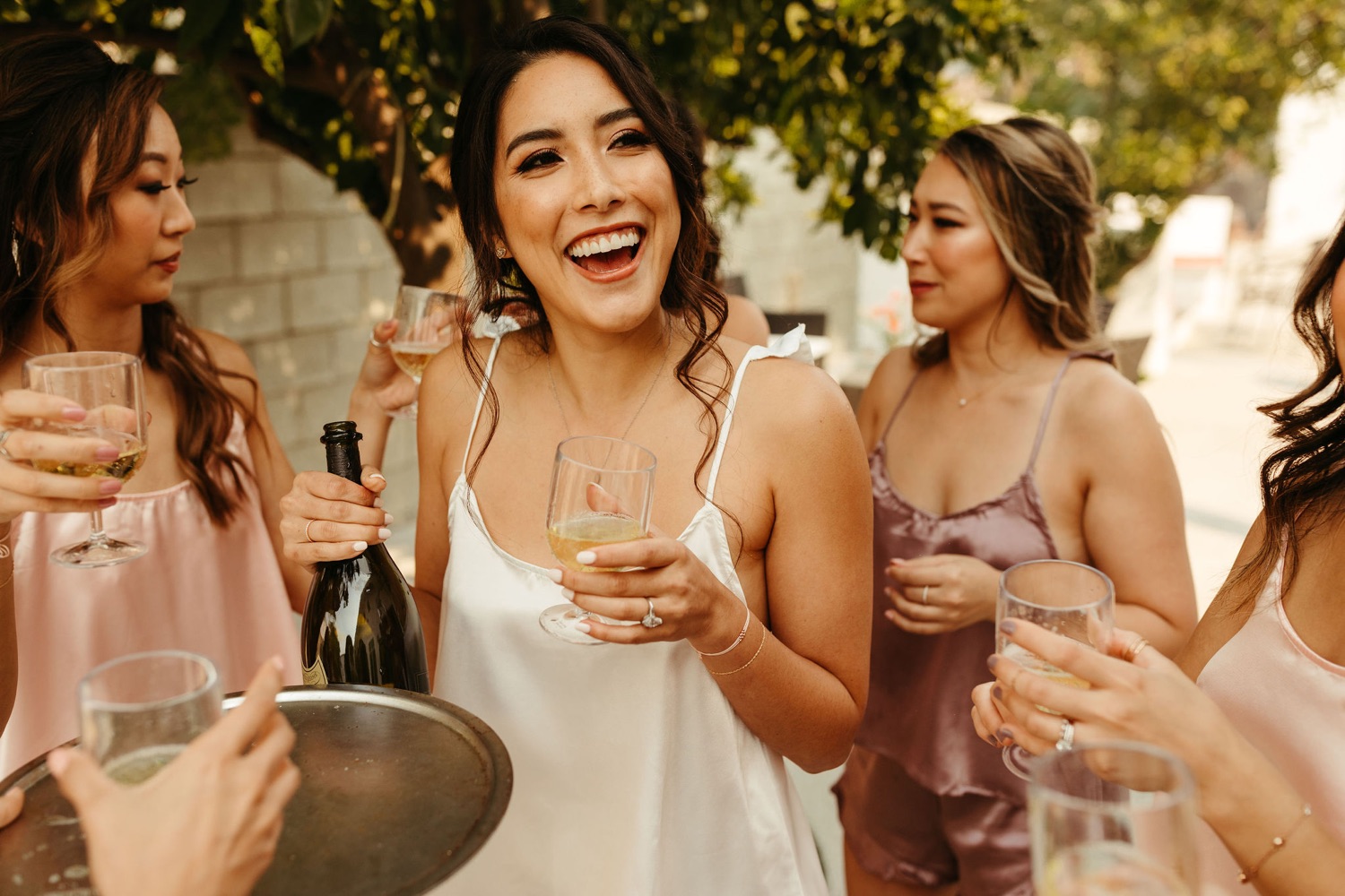 bridemaids getting ready in matching silk pjs popping champagne