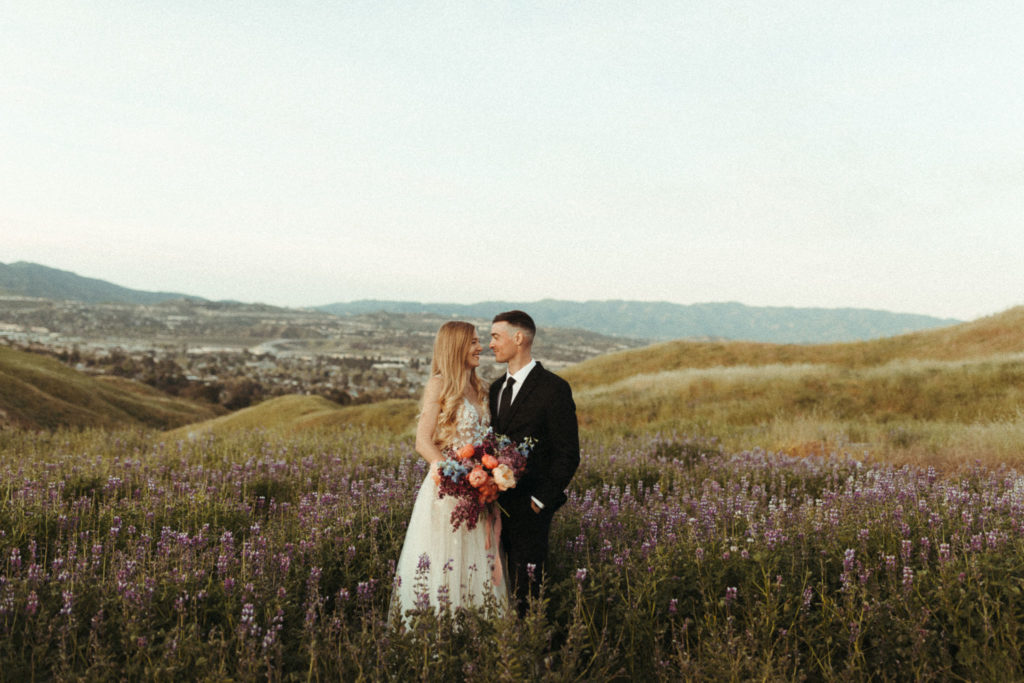 gorgeous bride and groom celebrating their wedding elopement at sunrise in some lupine fields with a beautiful romantic floral bouquet