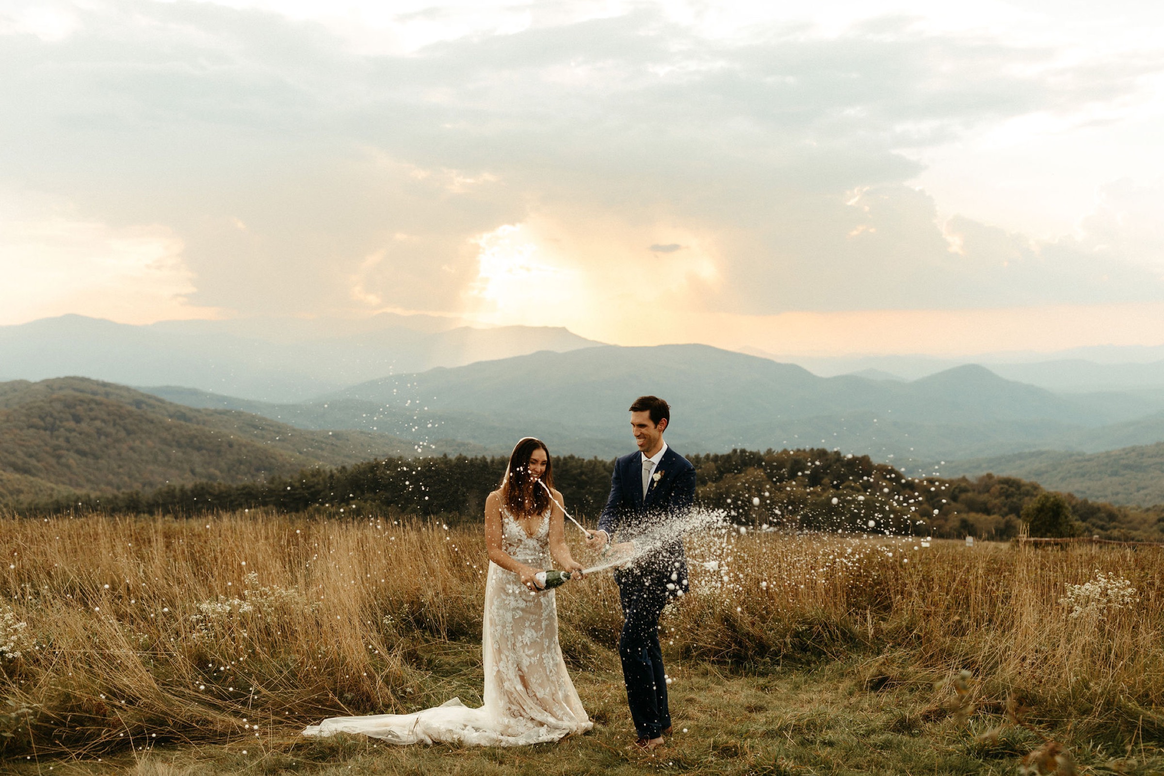 bride and groom popping champagne on a mountain