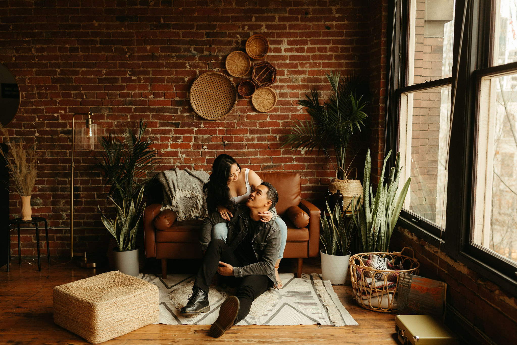couple sitting in their Seattle loft with exposed brick walls, modern interior design, leather sofa, and lots of plants
