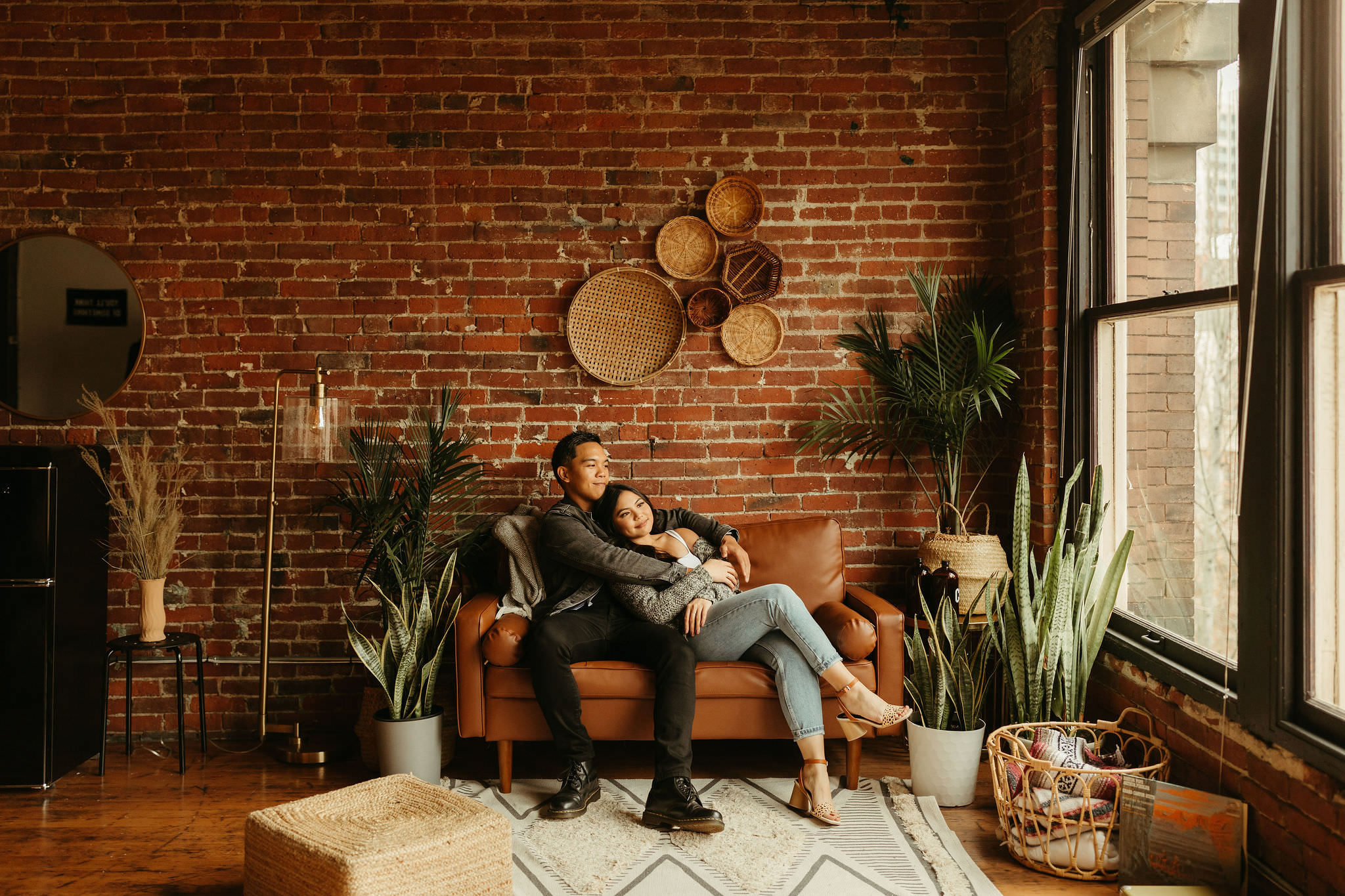 couple cozying up on their leather couch in their Seattle loft featuring exposed brick and huge windows and natural light