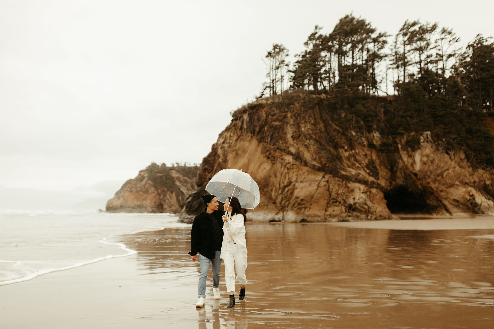 couple with clear umbrella running around the Oregon Coast on a rainy day