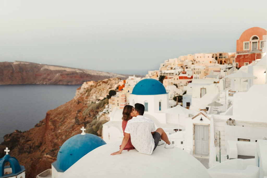 couple watching the sunrise in santorini on the roof of the blue and white houses