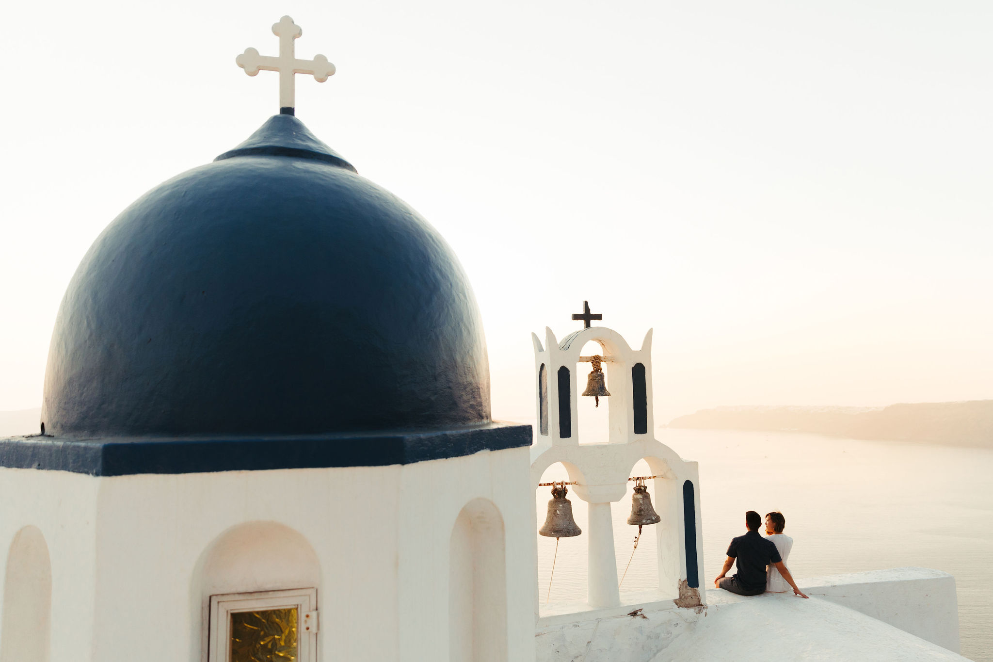 couple sitting on abandoned church watching sunset in oia santorini