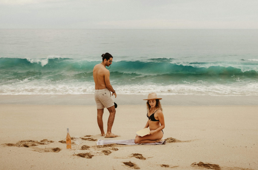 couple sets up for picnic on the beach in cabo with emerald green and blue water