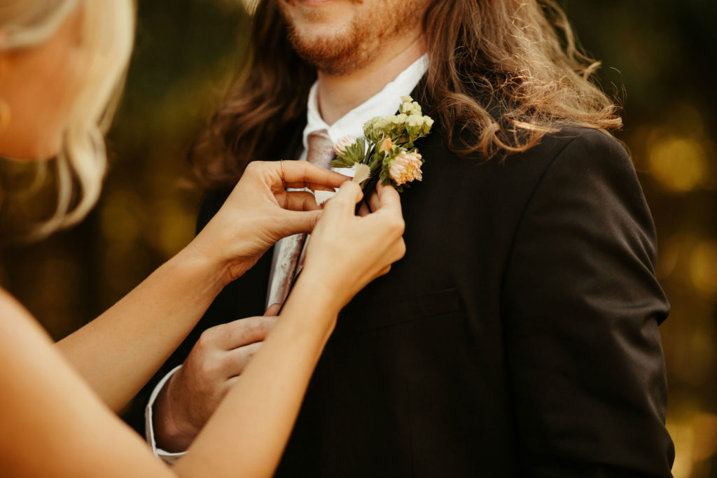 bride pins boutonniere on her groom